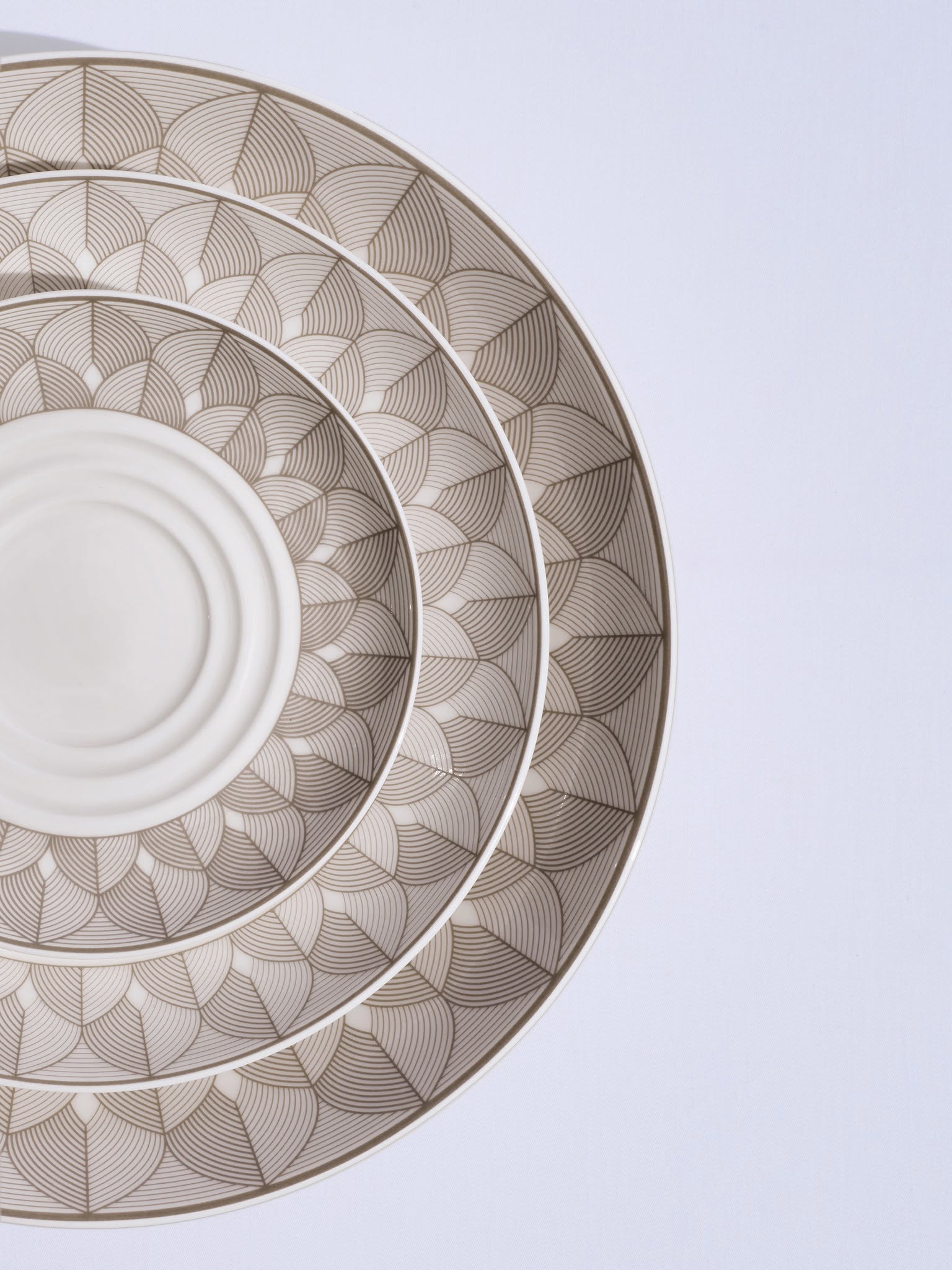 Three decorative plates stacked on top of each other, showcasing a leaf-like pattern in beige and white.