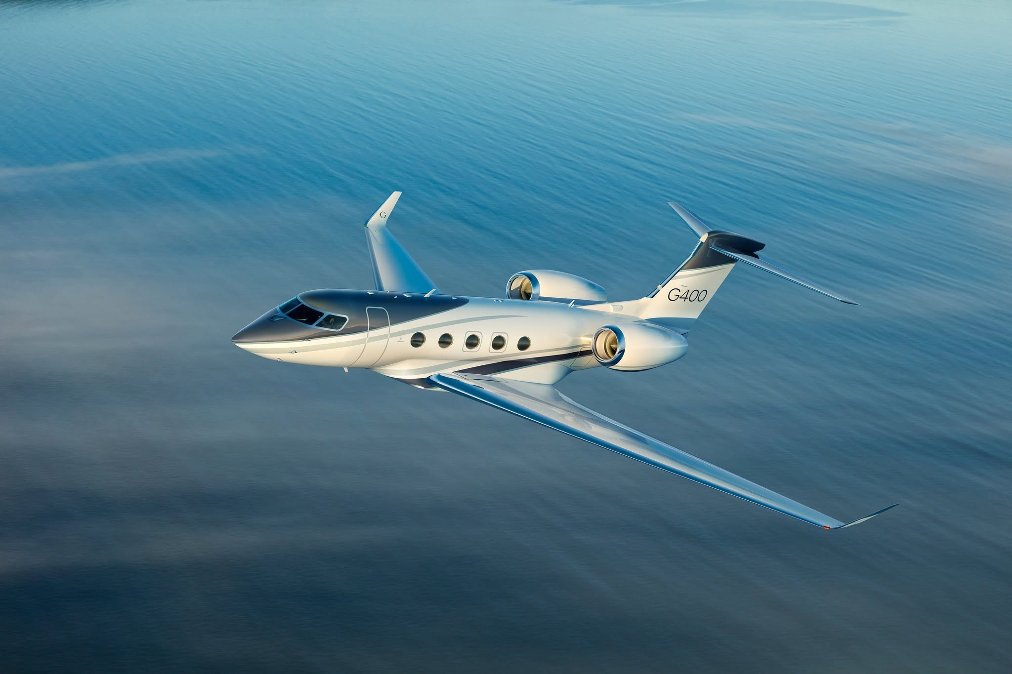 A sleek private jet, the G400, flying above calm blue waters under a clear sky.