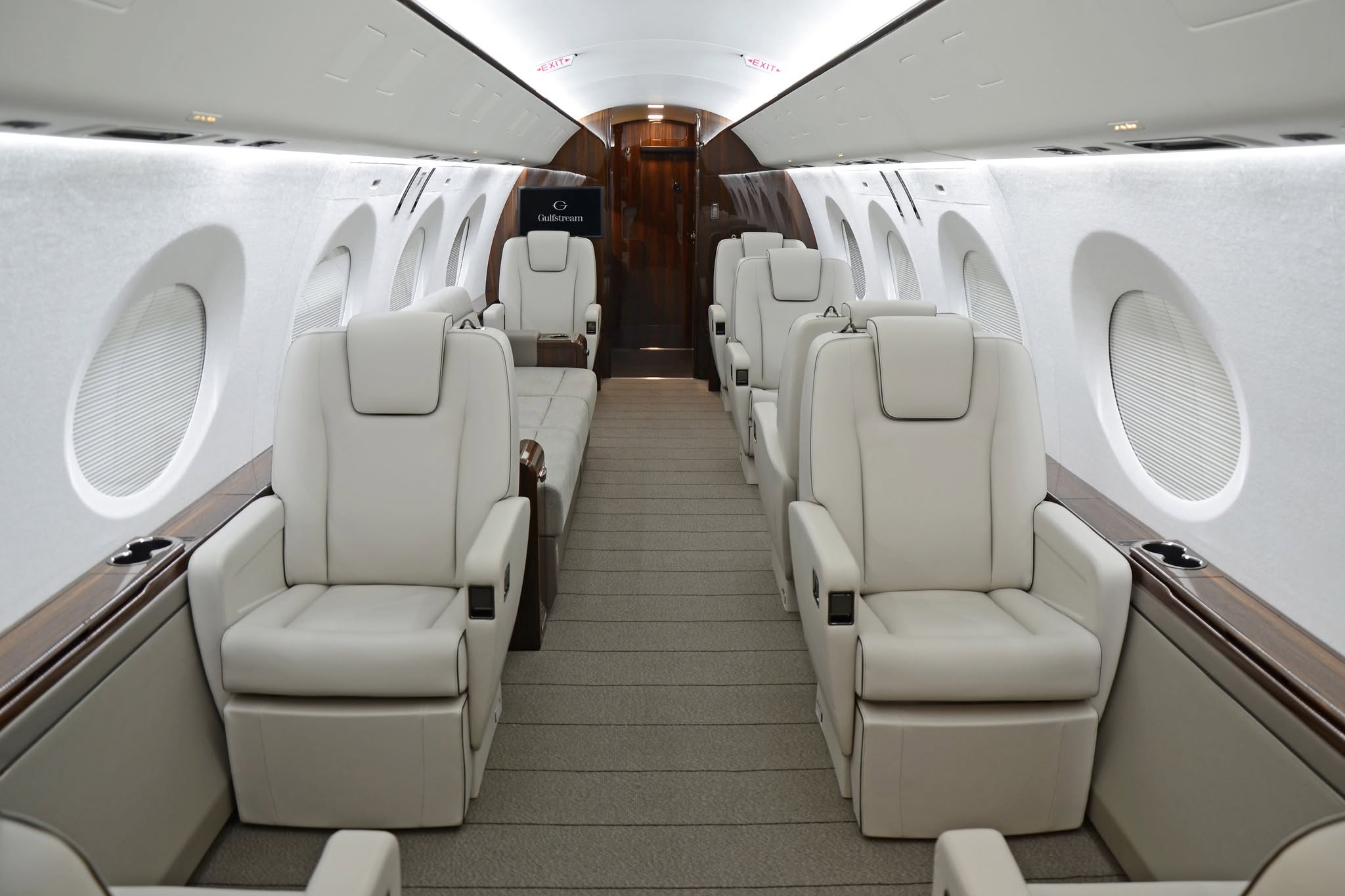 Interior of a luxurious private jet featuring plush white seating, wide aisles, and elegant decor.