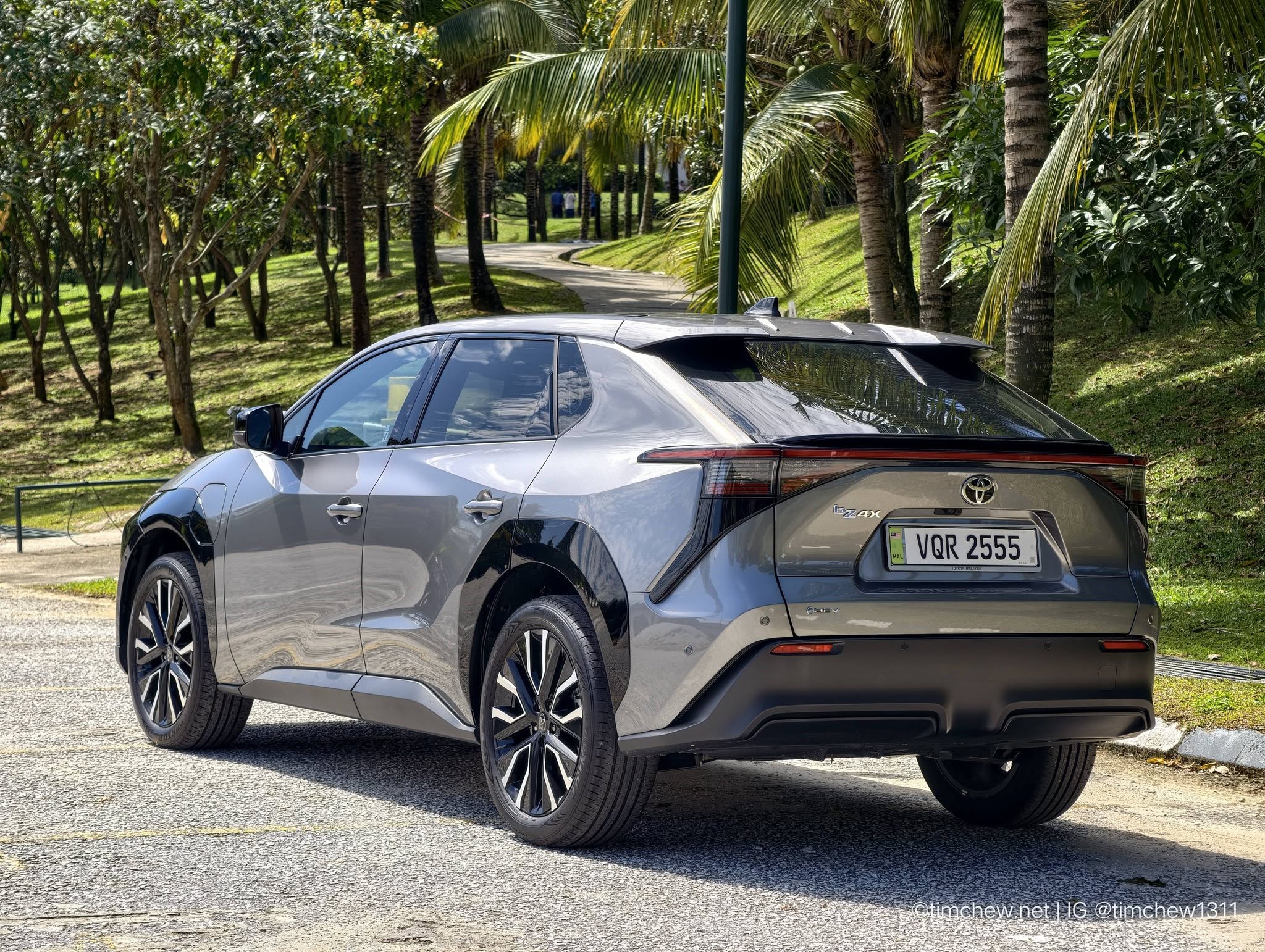 A gray Toyota vehicle parked in a lush green area with palm trees in the background, showing the rear and side profile.
